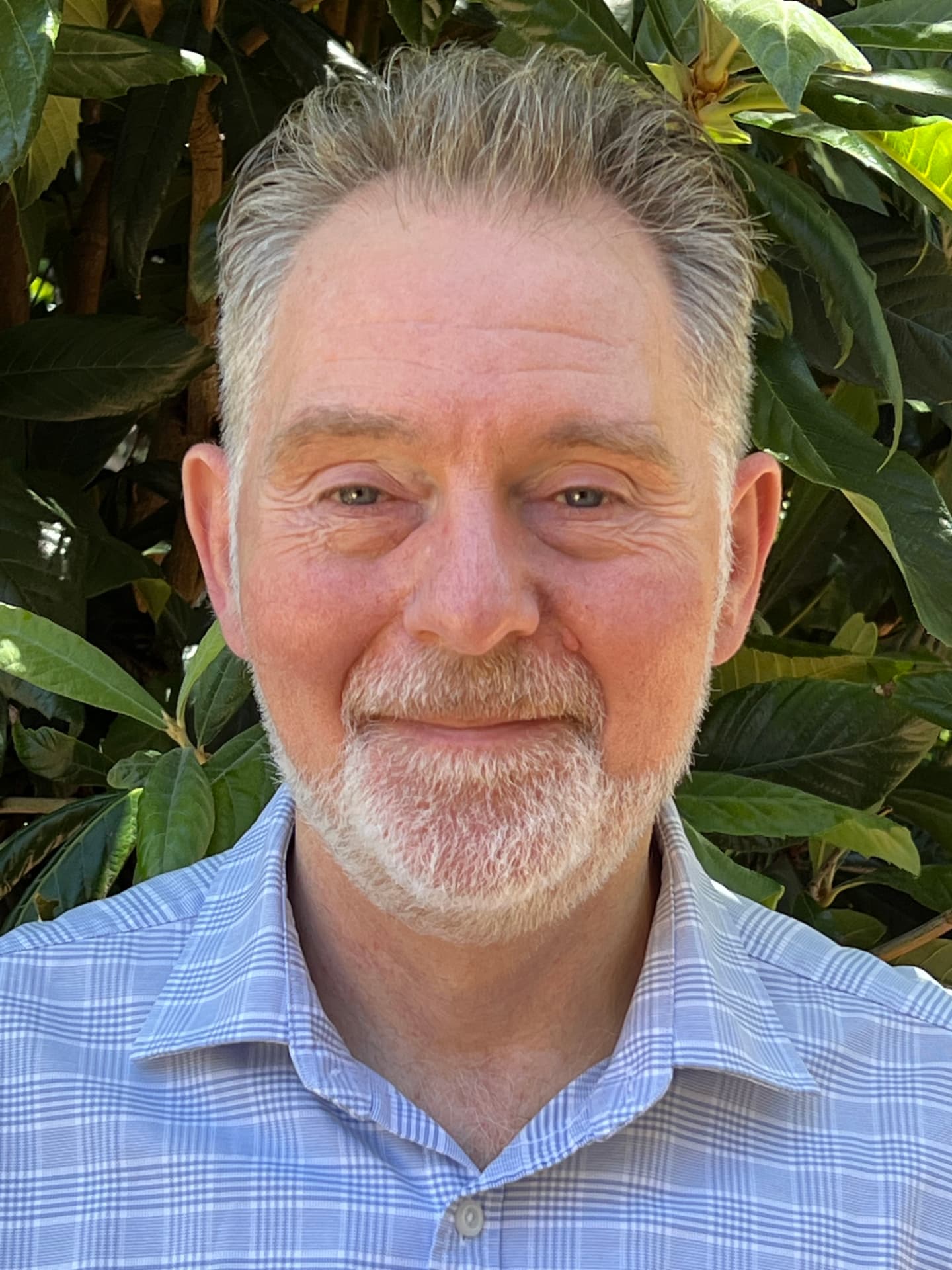 Tony Wittcomb, co-founder of Safety Coach International, in a light blue checked shirt with green foliage behind him.