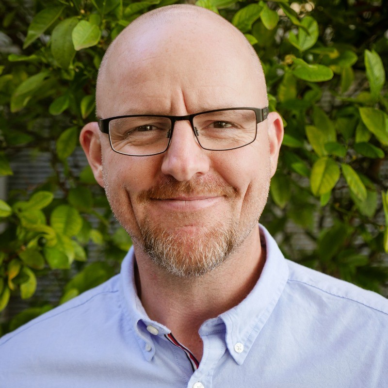 David Wollage, co-founder of Safety Coach International, smiling in a light blue shirt with greenery behind him.