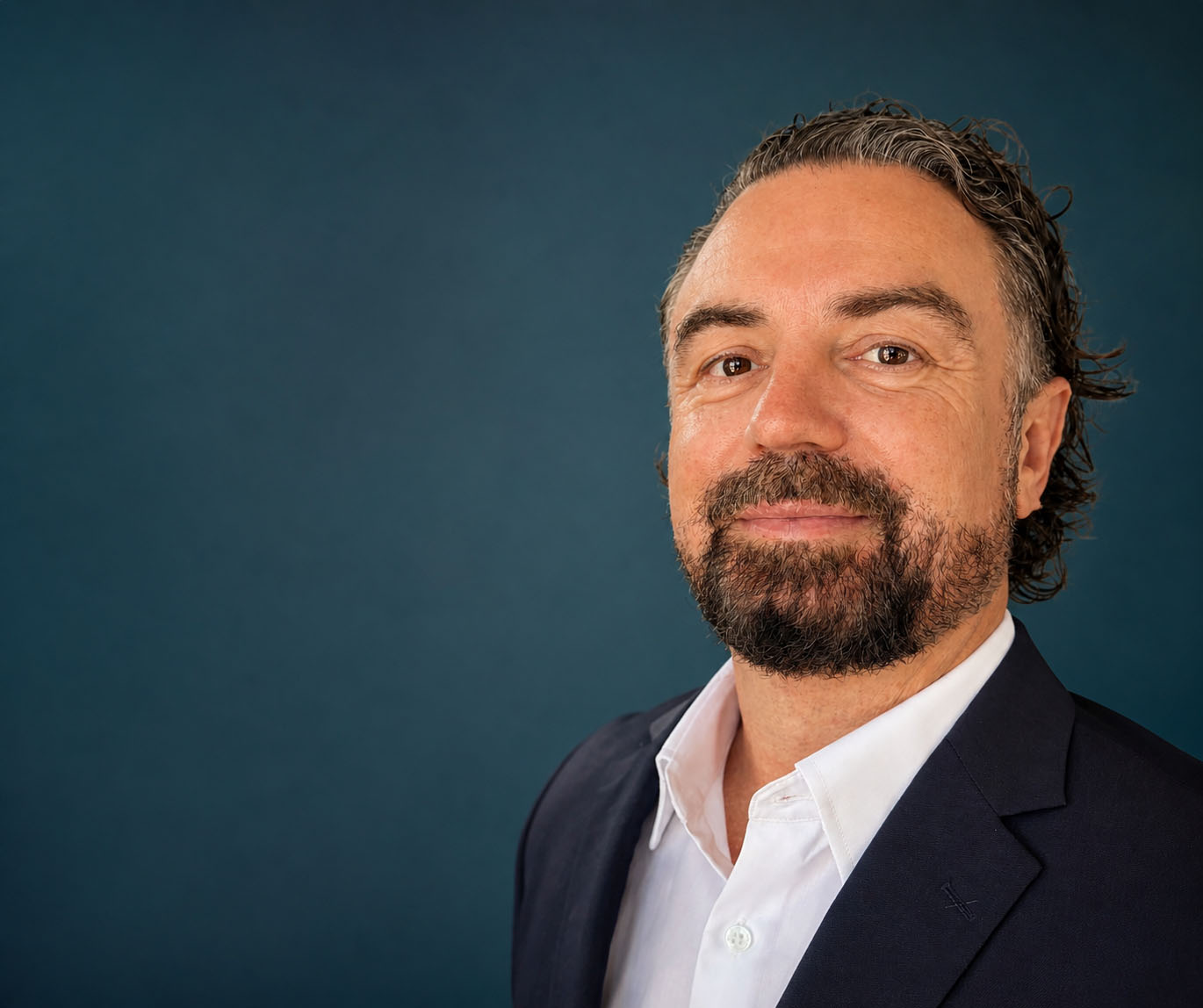 Ian Collins, co-founder of Safety Coach International, in a dark blazer and white shirt against a teal studio background.